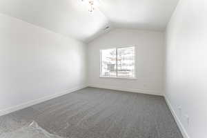 Carpeted empty room with a textured ceiling and vaulted ceiling