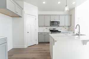 Kitchen featuring gray cabinetry, hanging light fixtures, stainless steel appliances, a breakfast bar, and tasteful backsplash