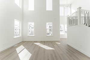 Unfurnished living room with a notable chandelier, light hardwood / wood-style floors, a towering ceiling, and a wealth of natural light