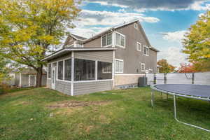 Rear view of property with cooling unit, a lawn, a trampoline, and a sunroom