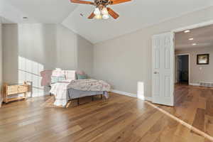 Bedroom featuring a walk in closet, hardwood / wood-style flooring, vaulted ceiling, and ceiling fan