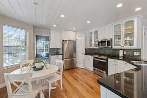 Kitchen featuring appliances with stainless steel finishes, light wood-type flooring, decorative backsplash, and white cabinets