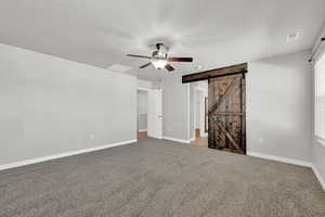 Unfurnished bedroom with a textured ceiling, a barn door, light colored carpet, and ceiling fan