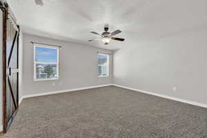 Carpeted bedroom with a textured ceiling, a barn door, and ceiling fan