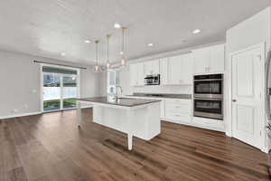 Kitchen featuring dark hardwood / wood-style floors, a kitchen breakfast bar, hanging light fixtures, a center island with sink, and appliances with stainless steel finishes