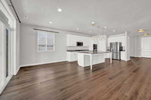 Kitchen featuring dark hardwood / wood-style floors, an island with sink, stainless steel appliances, decorative light fixtures, and white cabinets