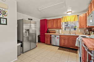 Kitchen featuring wooden counters, stainless steel appliances, sink, light tile patterned floors, and tasteful backsplash