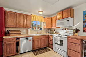 Kitchen with backsplash, sink, light tile patterned flooring, and white appliances