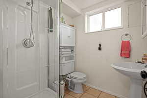 Bathroom featuring a shower with door, toilet, sink, and tile patterned flooring