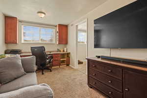 Home office with a textured ceiling, light colored carpet, and built in desk