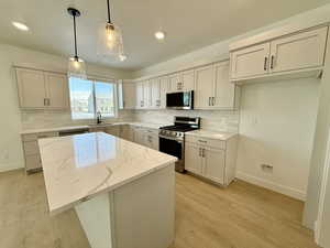 Kitchen with appliances with stainless steel finishes, light stone counters, sink, a center island, and hanging light fixtures