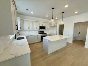 Kitchen with white cabinetry, sink, hanging light fixtures, stainless steel appliances, and a kitchen island