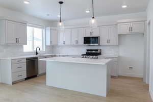 Kitchen featuring light hardwood / wood-style flooring, pendant lighting, decorative backsplash, a kitchen island, and appliances with stainless steel finishes