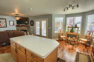 Kitchen featuring ceiling fan, a stone fireplace, a kitchen island, light wood-type flooring, and french doors