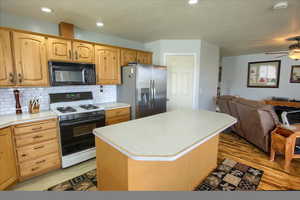 Kitchen featuring a kitchen island, white range with gas stovetop, stainless steel refrigerator with ice dispenser, decorative backsplash, and light hardwood / wood-style floors