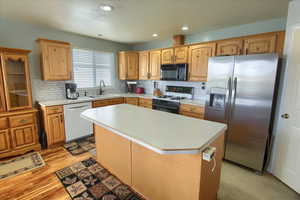 Kitchen featuring sink, backsplash, white appliances, a center island, and light wood-type flooring