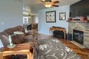 Living room with a fireplace, wood-type flooring, and ceiling fan