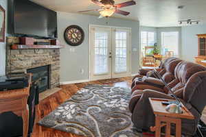 Living room featuring french doors, a textured ceiling, hardwood / wood-style flooring, ceiling fan, and a fireplace