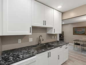 Kitchen featuring dishwasher, dark stone counters, sink, light wood-type flooring, and white cabinetry