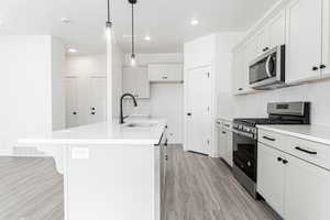 Kitchen featuring a center island with sink, stainless steel appliances, light wood-type flooring, and a sink