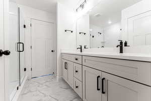 Bathroom featuring visible vents, double vanity, a sink, a shower stall, and marble finish floor