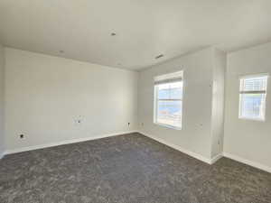 Unfurnished room featuring a healthy amount of sunlight and dark colored carpet