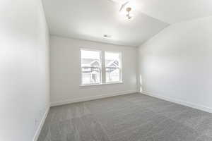 Carpeted empty room with visible vents, baseboards, and vaulted ceiling