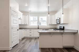 Kitchen with a breakfast bar area, wood finished floors, a peninsula, a sink, and appliances with stainless steel finishes