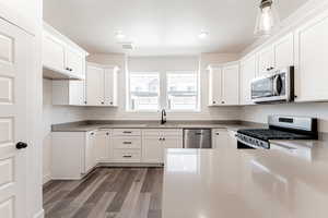 Kitchen with wood finished floors, appliances with stainless steel finishes, white cabinetry, and a sink