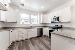 Kitchen with visible vents, a sink, appliances with stainless steel finishes, white cabinets, and light wood finished floors