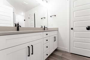 Full bathroom with double vanity, wood finished floors, baseboards, and a sink