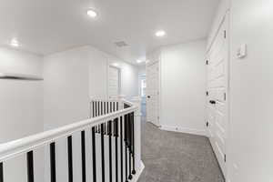 Corridor with carpet, visible vents, baseboards, recessed lighting, and an upstairs landing