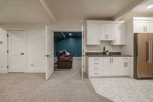 Kitchen featuring white cabinetry, light carpet, sink, and stainless steel fridge