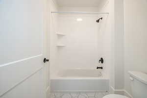 Bathroom featuring tiled shower / bath, tile patterned floors, and toilet