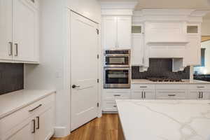 Kitchen with light hardwood / wood-style flooring, stainless steel appliances, backsplash, and white cabinetry