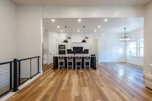 Kitchen featuring a kitchen bar, a large island, light hardwood / wood-style floors, white cabinetry, and decorative light fixtures