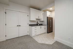 Kitchen featuring white cabinetry, stainless steel fridge, light colored carpet, and sink