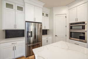 Kitchen with stainless steel appliances, light stone countertops, tasteful backsplash, and white cabinets