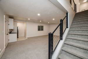 Staircase featuring a textured ceiling, sink, and carpet flooring