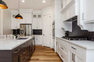 Kitchen with appliances with stainless steel finishes, white cabinets, sink, and hanging light fixtures