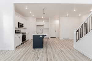 Kitchen featuring visible vents, an island with sink, a sink, stainless steel appliances, and light wood finished floors