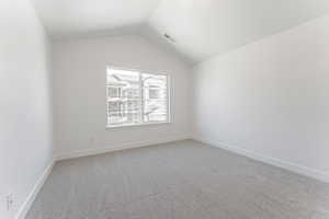 Empty room featuring baseboards, visible vents, lofted ceiling, and light carpet