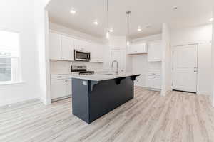 Kitchen with an island with sink, a sink, appliances with stainless steel finishes, white cabinetry, and a kitchen breakfast bar