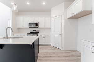 Kitchen with decorative light fixtures, light wood-style flooring, white cabinets, stainless steel appliances, and a sink