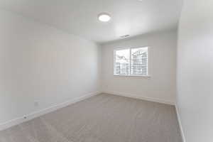 Empty room featuring a textured ceiling, baseboards, visible vents, and light carpet
