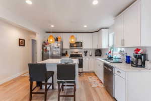 Kitchen featuring appliances with stainless steel finishes, light wood-type flooring, a kitchen island, hanging light fixtures, and white cabinets