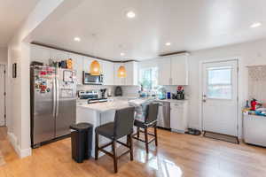 Kitchen featuring a kitchen island, light hardwood / wood-style flooring, stainless steel appliances, pendant lighting, and white cabinetry