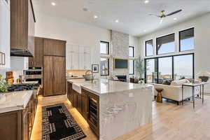 Kitchen with beverage cooler, an island with sink, light hardwood / wood-style flooring, a towering ceiling, and sink