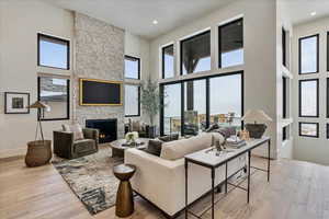 Living room featuring light hardwood / wood-style floors, a stone fireplace, and a towering ceiling