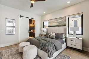 Bedroom with light hardwood / wood-style floors, a barn door, ensuite bath, and ceiling fan